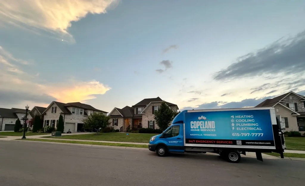 A blue Copeland Home Services van is parked on a suburban street in front of several houses at sunset.