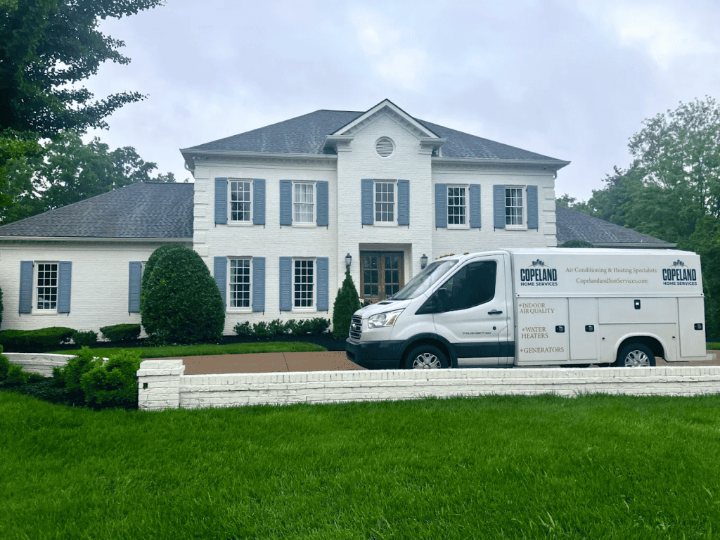 A white service van labeled “Copeland” is parked in front of a two-story white brick house with green landscaping and a white brick wall in Brentwood.